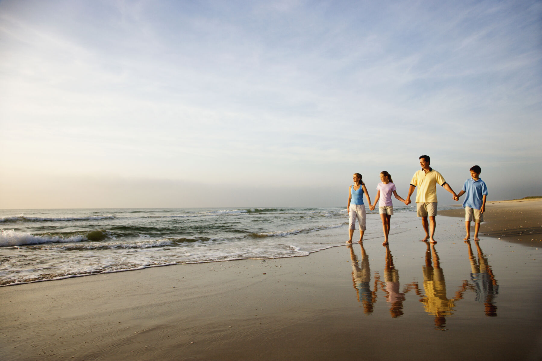 family of four holding hands on the beach